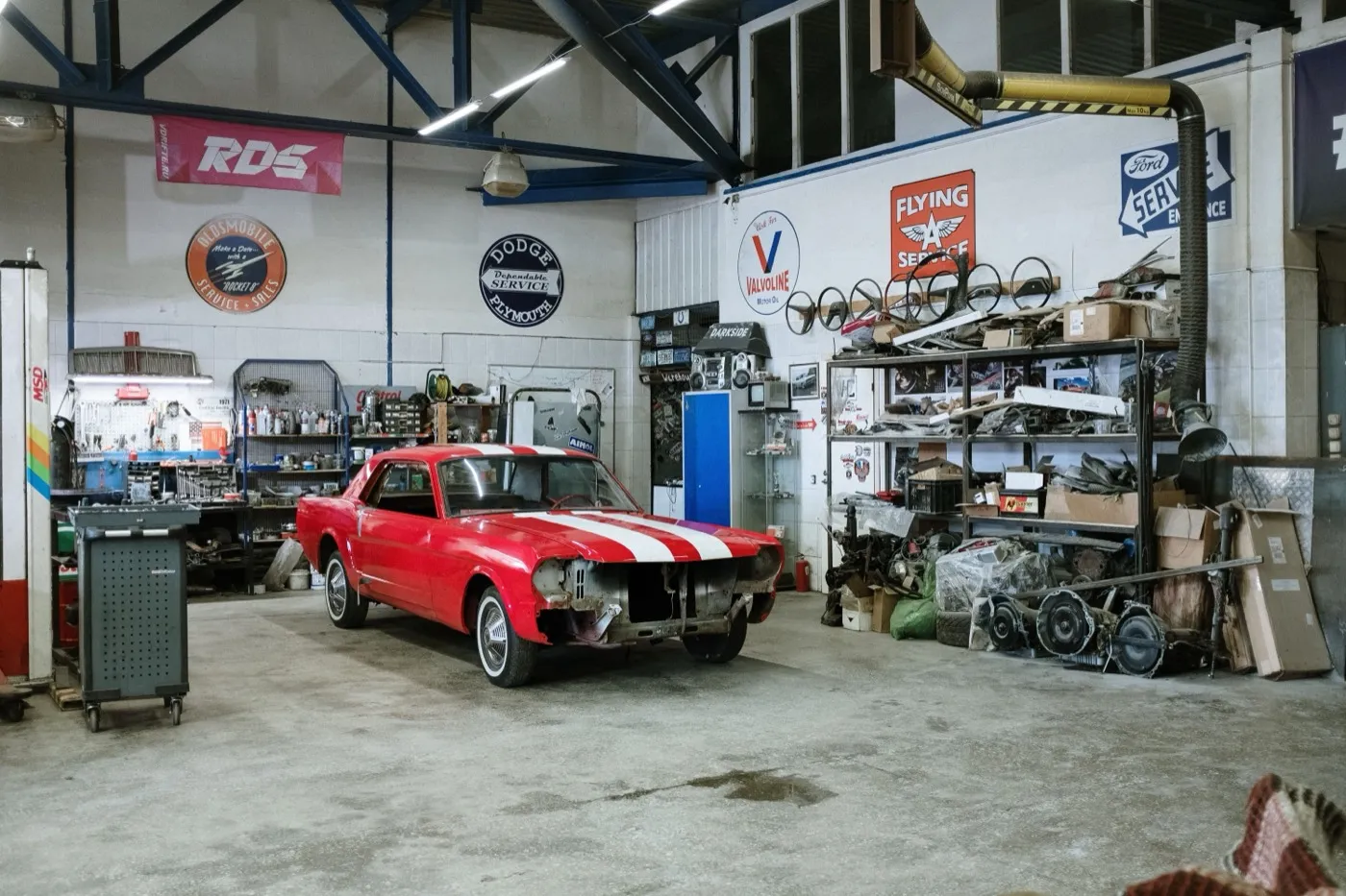 Roter Sportwagen in einer Werkstatthalle zwischen Werkzeugwagen und Ersatzteilregalen.