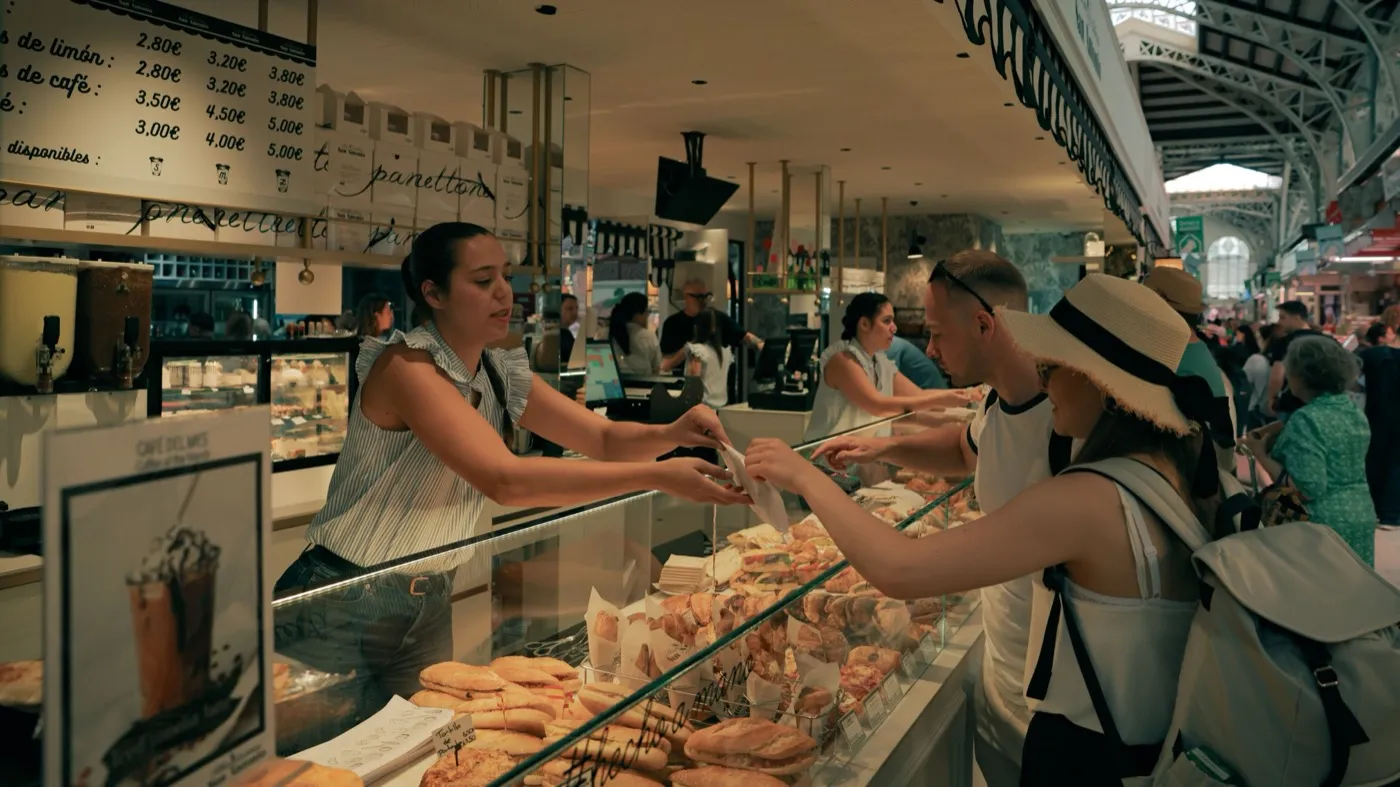 Una dependienta entrega su compra a una clienta por encima del mostrador lleno de una panadería.