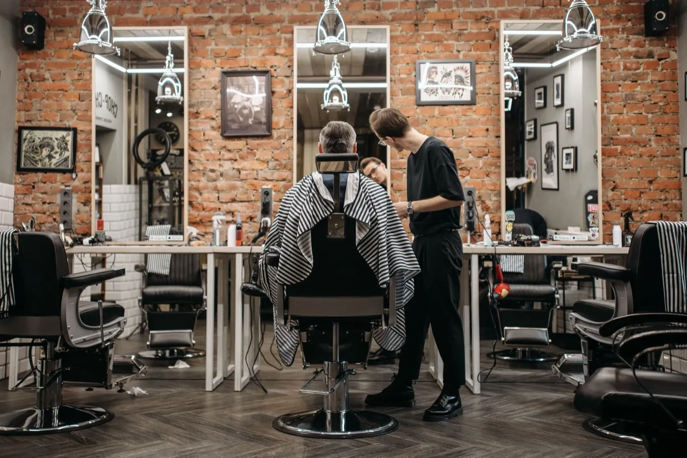 A barber at work in a barbershop with brick walls and mirrors.