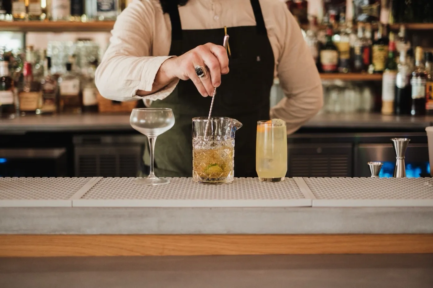 A bartender stirring a cocktail in a mixing glass behind the bar.