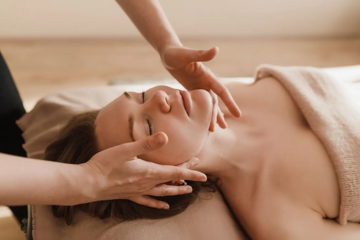 Une esthéticienne réalise un soin du visage pendant que la cliente est allongée, détendue, sur la table de soin.