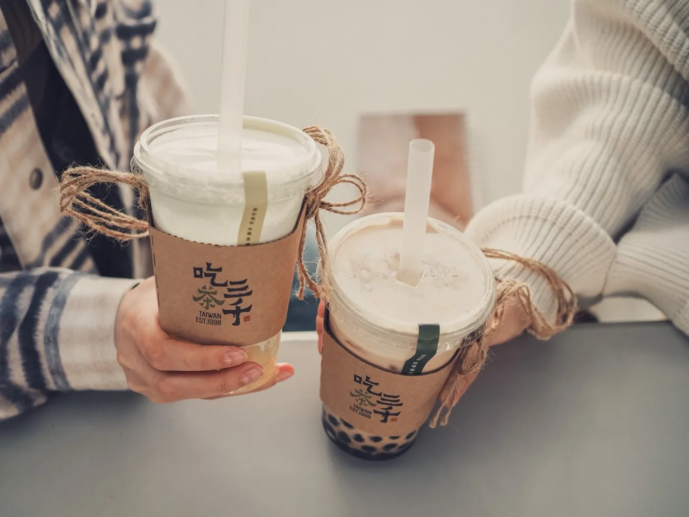 Zwei Hände halten Bubble-Tea-Becher mit Strohhalm und Tapioka-Perlen.
