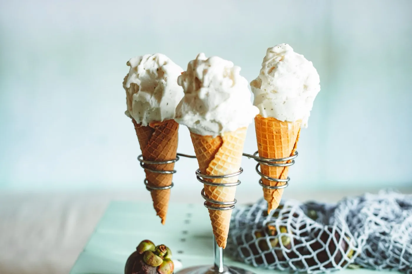 Tres cucuruchos con bolas de helado de colores claros en un soporte metálico.