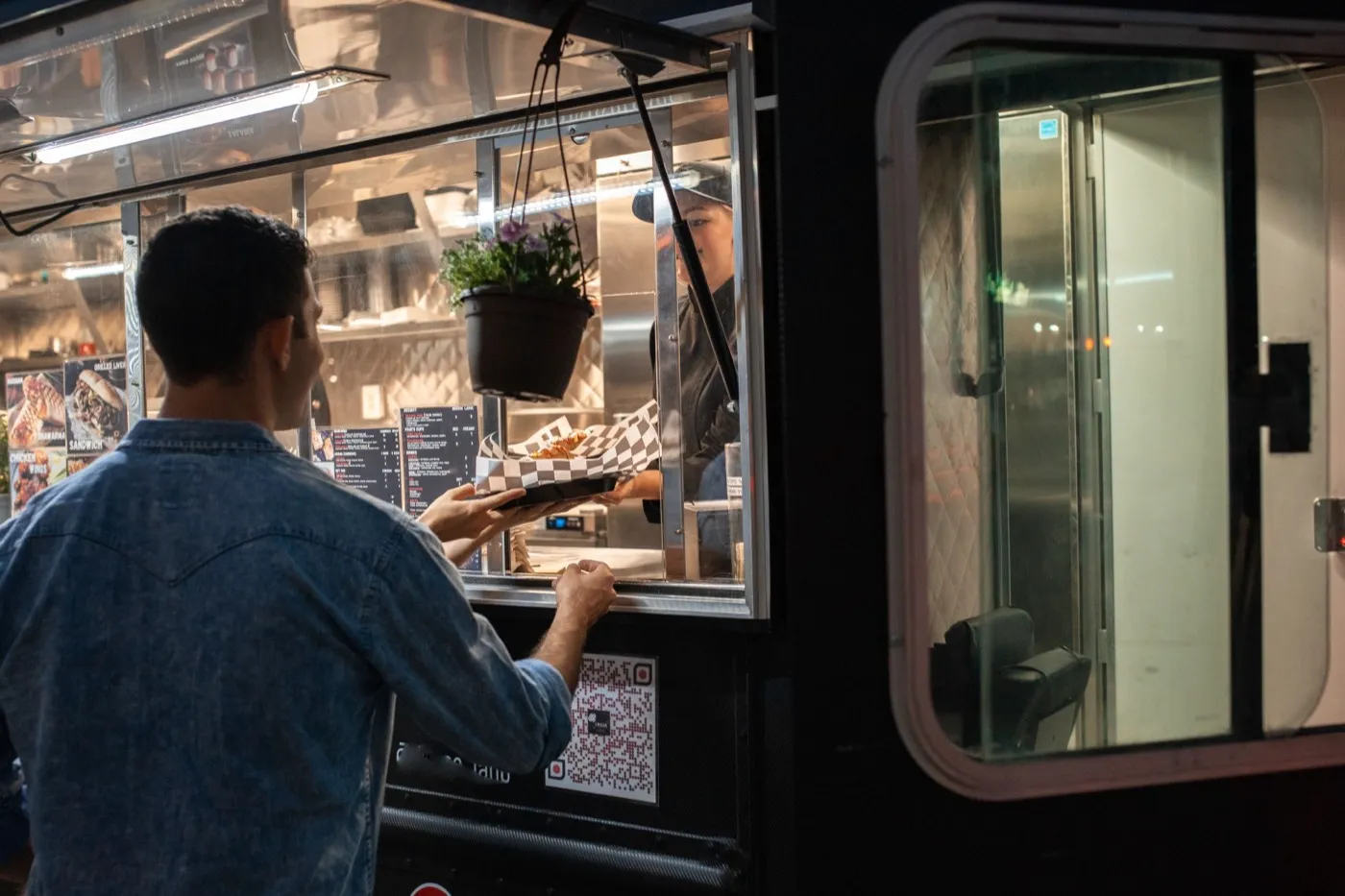 Ein Kunde bekommt am beleuchteten Fenster eines Foodtrucks sein Essen gereicht.