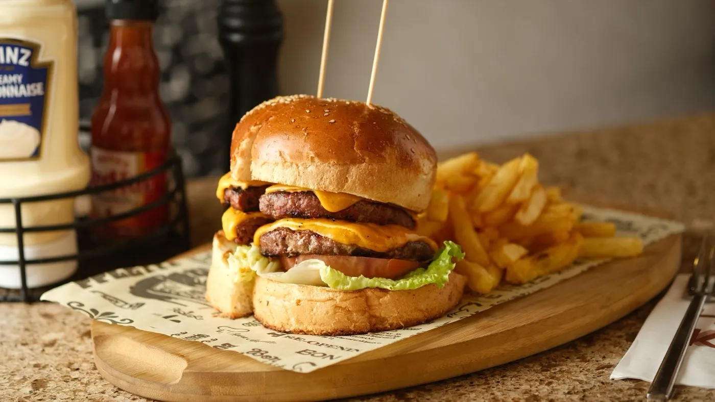 Ein Burger mit Pommes auf einem Holzbrett, daneben Ketchup und Mayonnaise.