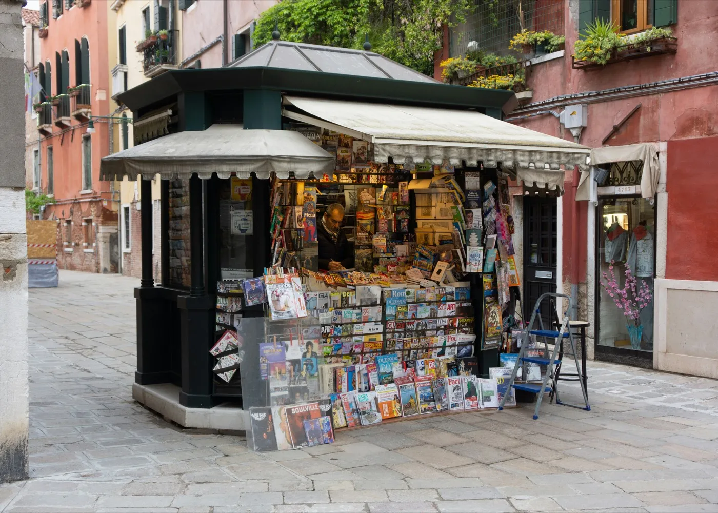 Kiosk auf einem Platz, Zeitschriften und Postkarten hängen vor dem Verkaufsfenster.