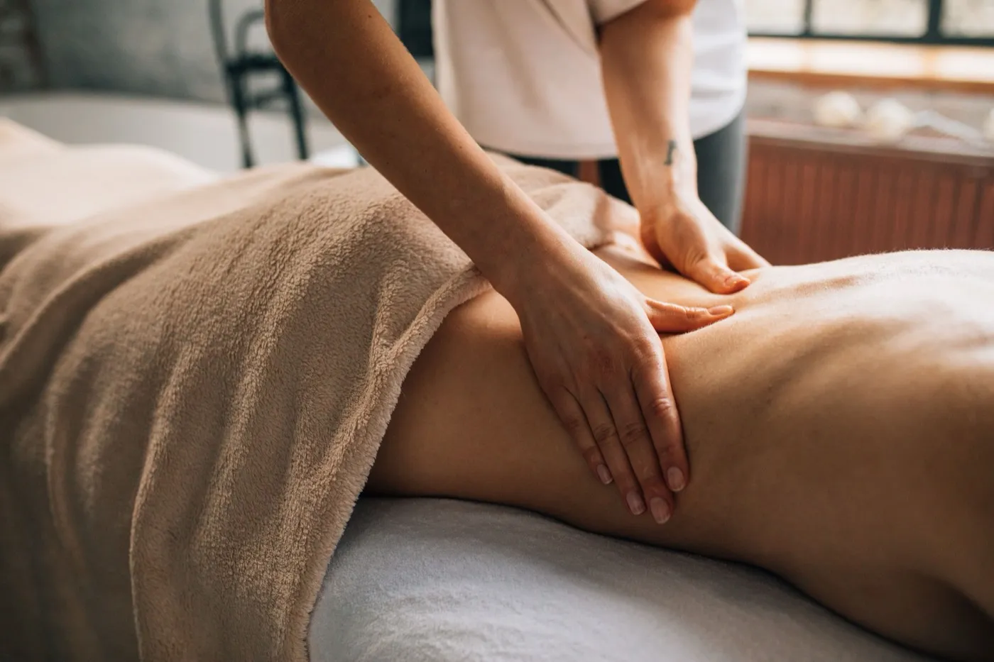 Masseurin massiert das Bein einer Kundin auf der Massageliege.