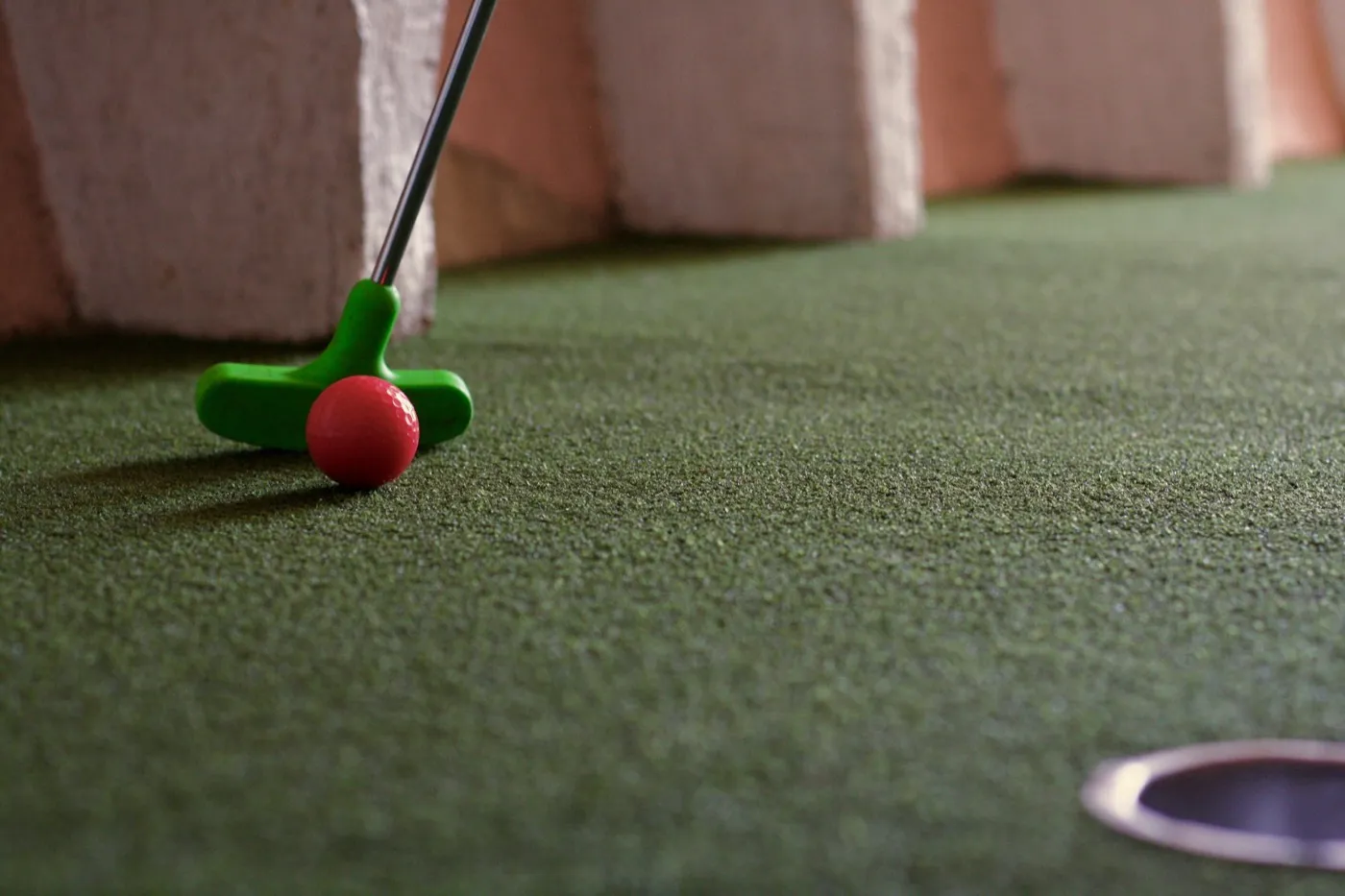 Grüner Minigolfschläger trifft einen roten Ball kurz vor dem Loch.