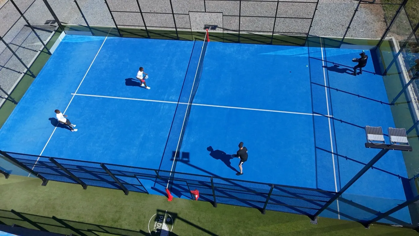 Blick von oben auf einen blauen Padel-Court mit vier Spielern im Spiel.