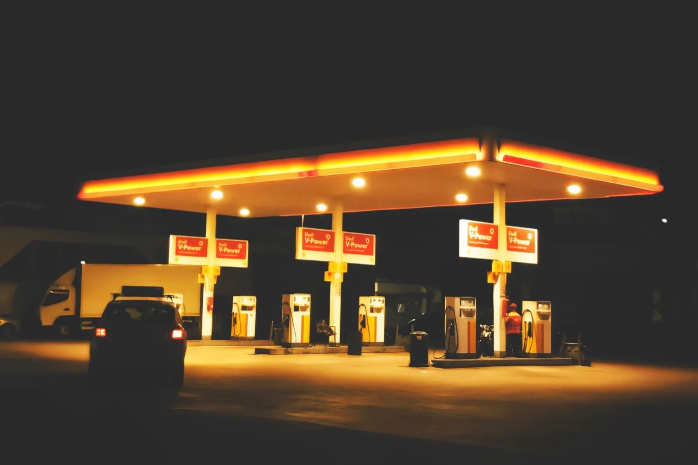 Beleuchtete Tankstelle bei Nacht, ein Auto steht an der Zapfsäule.