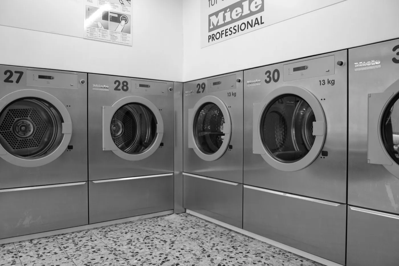 Reihe großer, nummerierter Waschmaschinen in einem Waschsalon.