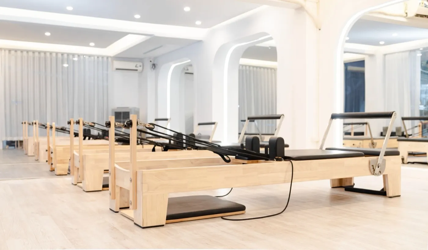 Heller Pilatesraum mit einer Reihe Reformer-Geräten aus hellem Holz.